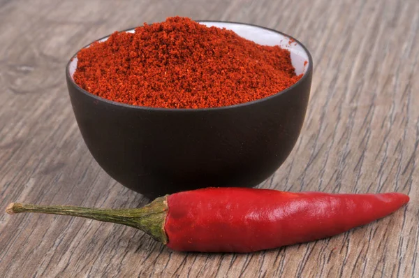 Bowl of chili powder and red chili peppers close-up on wooden background