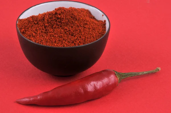 Bowl of chili powder and red chili peppers close-up on red background