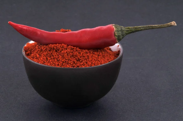 Bowl of chili powder and red chili peppers close-up on black background