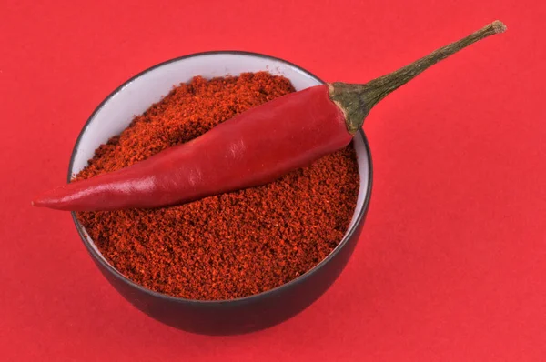 Bowl of chili powder and red chili peppers close-up on red background