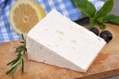 Bıçaklı, siyah zeytinli, limonlu ve biberiyeli kesme tahtasındaki bir parça feta.