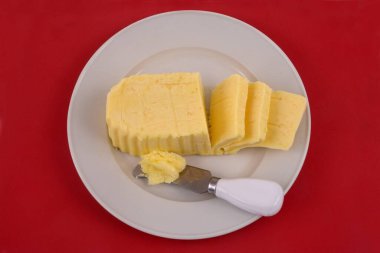 Bir tabakta tereyağı, yukarıdan görünen bir bıçakla kırmızı arka planda.