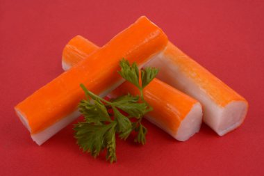 Surimi çubukları kırmızı arka planda maydanozdan bir filizle üst üste yığılmış.