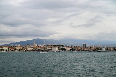 Suyun üstünde yelkenlisi ve bulutlu gökyüzü olan Split şehrinin genel manzarası