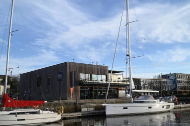 Vannes marinasındaki rıhtıma demirlemiş yelkenliler ve arka planda liman müdürünün ofisi var.