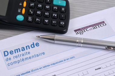 Yakın planda gösterilen bir hesap makinesi ve kalemle Agirc-Arrco tamamlayıcı emeklilik başvuru formu