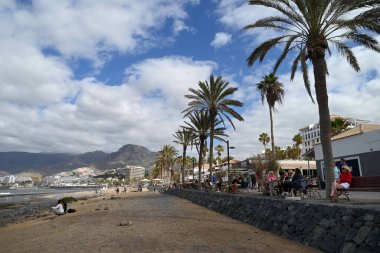 Arka planda kentsel ve dağlık bir manzaraya sahip Tenerife adasındaki Las Amerika plajındaki turistler