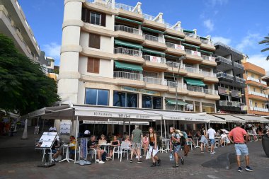 Tenerife adasındaki Los Cristianos 'ta bar ve restoranlarla dolu Paseo Maritimo boyunca gezinen turistler