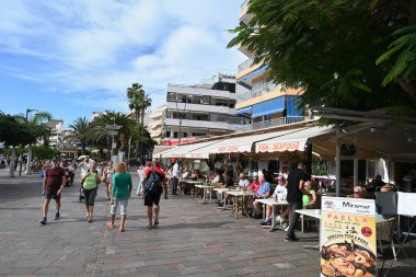 Tenerife adasındaki Los Cristianos 'ta bar ve restoranlarla dolu Paseo Maritimo boyunca gezinen turistler
