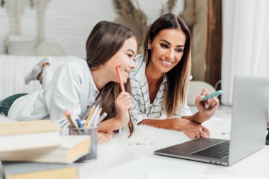 Gülümseyen esmer kadın kızına ödevlerinde yardım ediyor..