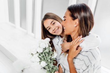 Çocuk annesine sarılıyor gülümsüyor ve kameraya bakıyor.