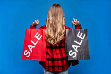 Arka planda mavi arka planda sıradan giyinmiş genç sarışın bir kız, bir paket, sonbahar indirimi.