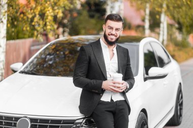 Arabanın arka planında başarılı bir genç adam. Elinde kahve ve sarı yapraklarla arka planda..