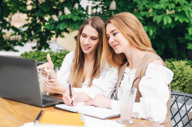 İki kız kardeşin el ele tutuşup kameraya gülümsediği bir fotoğraf. Biri elinde çiçeklerle.