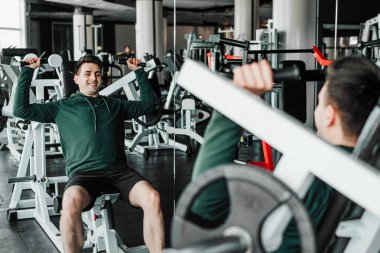 Yakışıklı kaslı adam spor salonunda omuz egzersizi yapıyor..