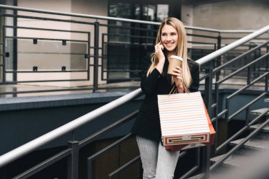 Başarılı bir işten sonra şık giyinmiş sarışın kahve içer ve telefonda gülümseyerek konuşur..