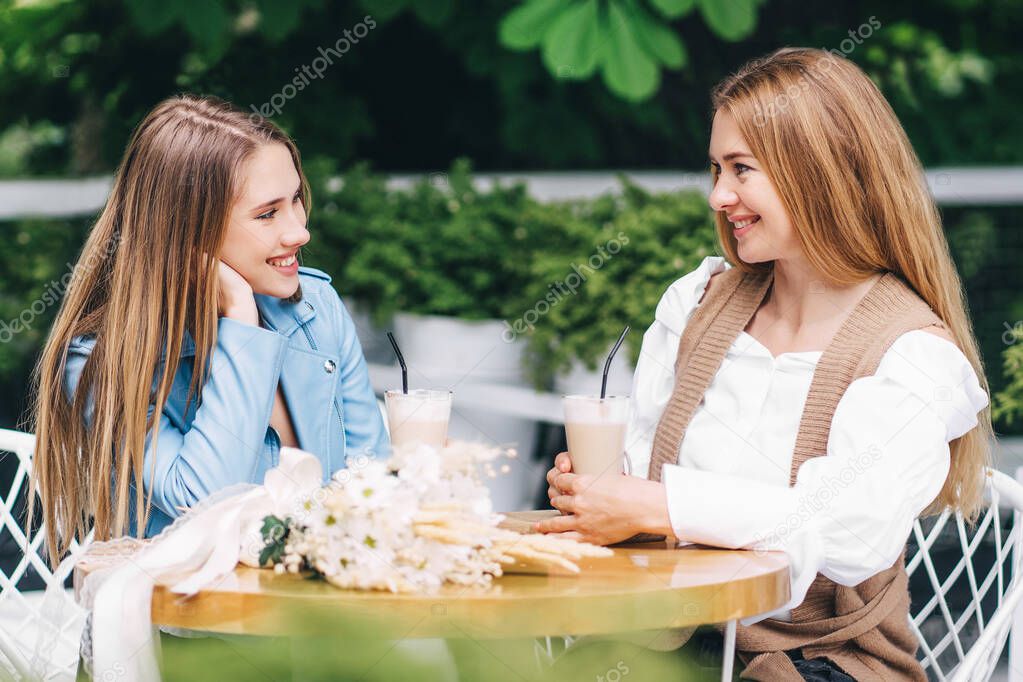 Portrait of mother and daughter smiling and looking at each other, sitting in a lounge and talking on the summer terrace.