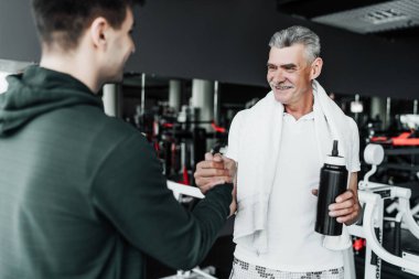 Yaşlı bir adamın portresi ve spor hocası, bir gülümsemeyle el sıkışıyorlar. Yaşlı adama odaklan..