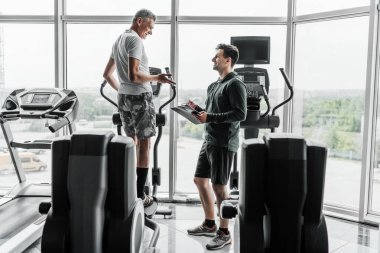 Kıdemli adam yörüngede egzersiz yapıyor ve spor hocasının tavsiyesini dinliyor..