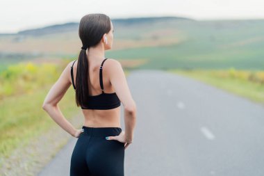 Yol geçmişinde elinde kulaklıklarla koşan atletik bir kadın..