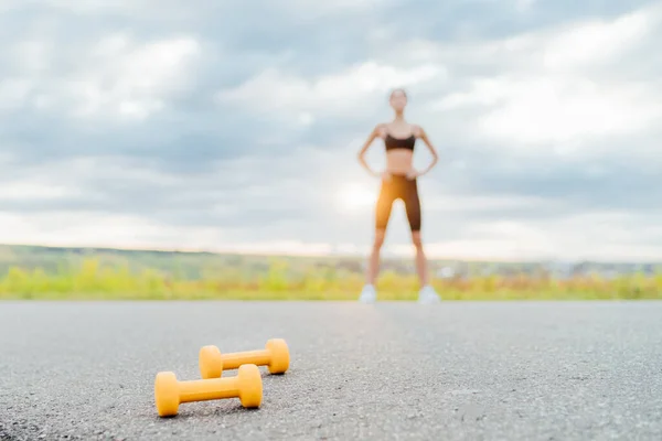 In the foreground dumbbells, in the background a blurred silhouette of a sports girl at dawn.