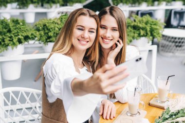 Güzel bir anne ve kız birlikte zaman geçiriyorlar. Bir kafede yaz terasında selfie çek..