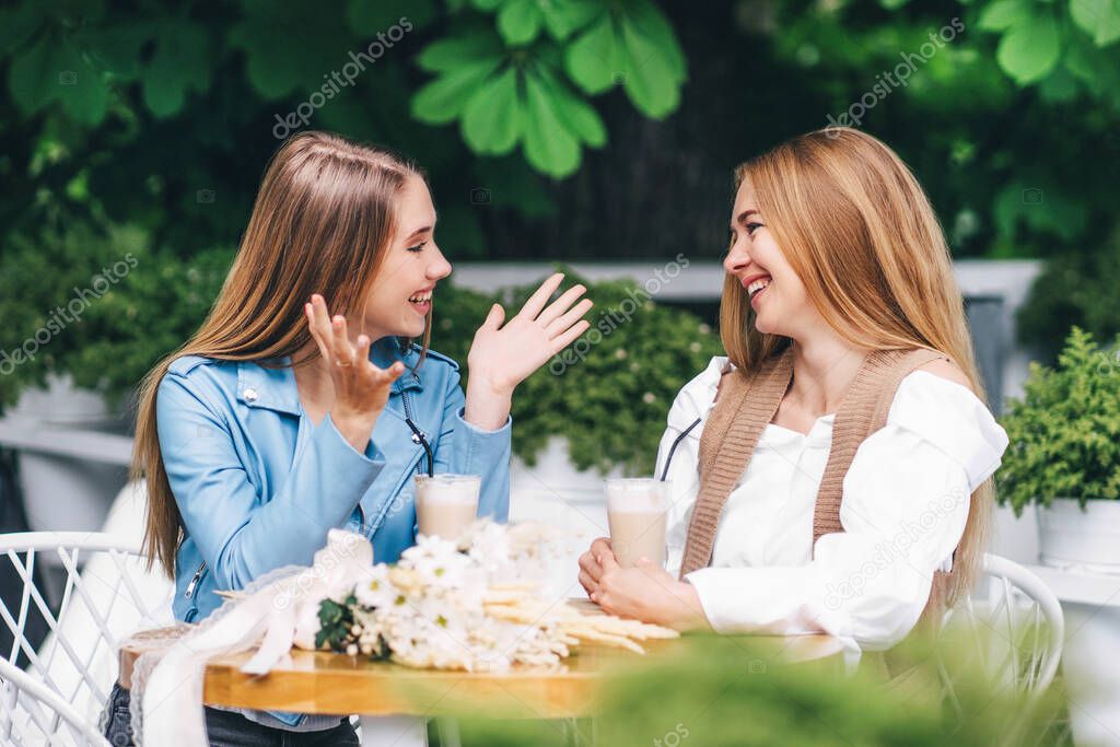 Two beautiful women are sitting at a table in a coffee shop and emotionally communicating, smiling at each other.