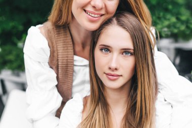 Çekici bir kızın portresi kameraya bakıyor, annesinin sarılmasının arkasında..