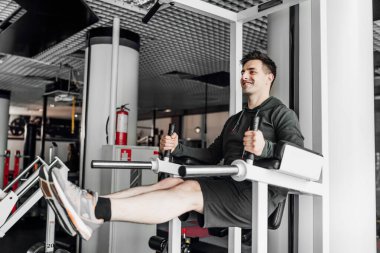 Genç yakışıklı adam spor salonunda bacaklarını kaldırarak basın açıklaması yapıyor..