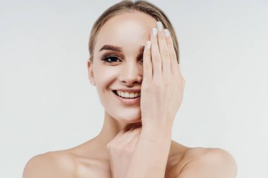 Beyaz arka planda çekici bir kadın kameraya gülümser ve komiklik elini eliyle kapatır. Sağlık ve cilt bakımı. Spa merkezi, kozmetoloji.