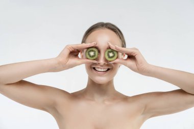 Beyaz arka plandaki komik kadın gözlerini kivi yarısıyla kapatıyor ve gülümsüyor. Stüdyo fotoğrafı. Spa.