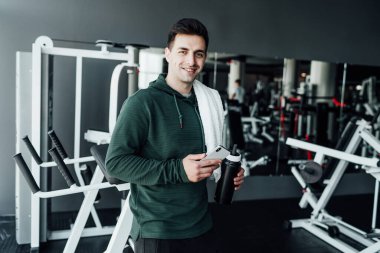 Spor salonunun ortasında antrenman yapmaya hazır yakışıklı bir adam duruyor ve gülümseyerek kameraya bakıyor. Spor salonunda genç bir koç. Sağlıklı Yaşam Tarzı.