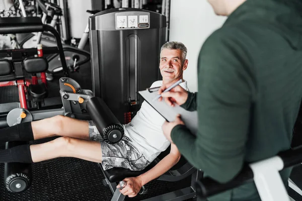 Konferansta simülatör üzerinde alıştırma yapan kıdemli adam, antrenörü eğitim planını ve sonuçları yazıyor. Rehabilitasyon koçu.