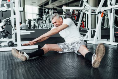 Spor salonunun zemininde, son sınıf emekli bir adam antrenmandan önce esniyor. Neşeli ve fiziksel olarak iyi durumda. Spor, yaşam ve sağlık.