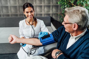 Gülümseyen bir hemşire yaşlı bir adamın kan basıncını ölçer ve gülümseyerek ona bakar. Doktorun eve ziyareti. Aile doktoru.