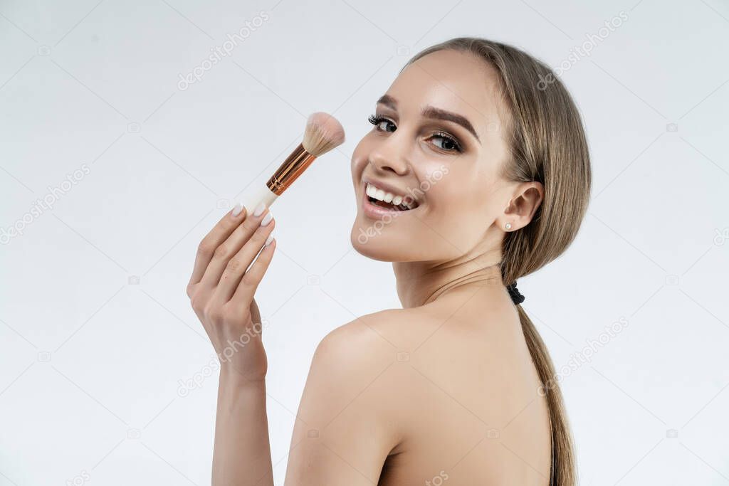 Lovely woman smiles and holds a make-up brush near her face. Natural makeup. Professional make-up artist.