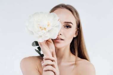 Parlak cilt, hassasiyet ve sağlık. Güzel kız beyaz arka planda narin beyaz bir çiçeğin yüzünü örtüyor. Spa, güzellik salonu.