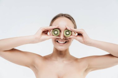 Işıl ışıl cildi olan bir kadının portresi dilimlenmiş bir kivinin yüzünü komik bir şekilde kapatıyor. Kişisel bakım, doğal cilt bakım ürünleri.