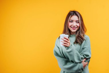 Sarı arka planda mesaj atmak için yer var. Elinde kahveyle gülümseyen tatlı kız kameraya bakıyor..