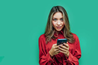 Elinde telefon olan çekici bir kız, kameraya bakmakla ilgileniyor, mesaj atabileceği bir yer..