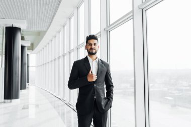 Modern bir ofisin ortasında yakışıklı, sakallı, Hintli bir işadamı kameraya bakar..