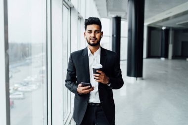 Modern bir binanın ortasında başarılı bir Hintli adam kameraya bakar ve elinde bir telefon tutar, patron..