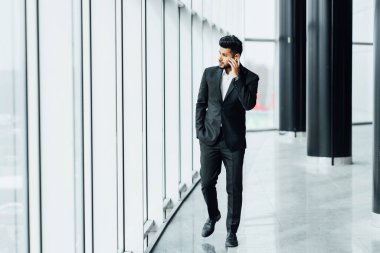 Meşgul bir Hintli işadamı modern bir binanın koridorunda yürüyor ve telefonla konuşuyor, bir iş toplantısına gidiyor, başarılı bir Hintli adam..