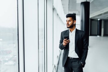 Ciddi sakallı bir Hintli modern telefonunu kullanıyor. Modern bir binanın ortasında siyah bir takım elbise giyiyor. Bir ofis çalışanı, bir patron, bir müdür..