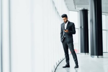 Modern bir binanın ortasında sakallı, yakışıklı Hintli bir adam takım elbiseli, telefonda konuşuyor, iş görüşmesi yapıyor..