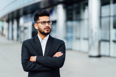 Modern Hintli bir ofis çalışanı, sakallı, yakışıklı bir Hintli, arkasında modern bir ofis binası var..