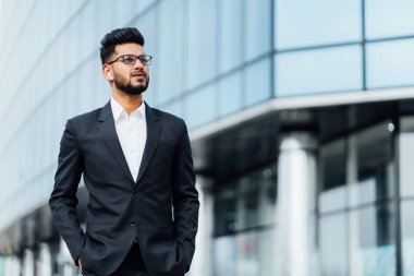 Siyah takım elbiseli çekici Hintli adam, arkasında modern bir ofis binası, Hintli bir işadamı..