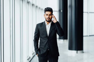 Asyalı sakallı bir adam, siyah takım elbiseli Hintli bir erkek avukat kablosuz kulaklıklara dokunuyor ve kameraya bakıyor..