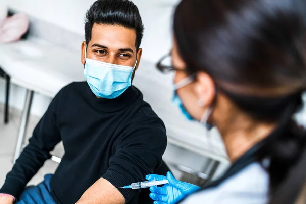 Smiling Indian male patient during vaccination, he smiles and looks at the doctor. Vaccination against code 19, protection and safety for health.