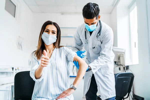 Vaccination of the patient, the doctor in a protective mask injects the vaccine into the patient\'s hand, it shows the camera okay, vaccination against coronavirus, health and safety.